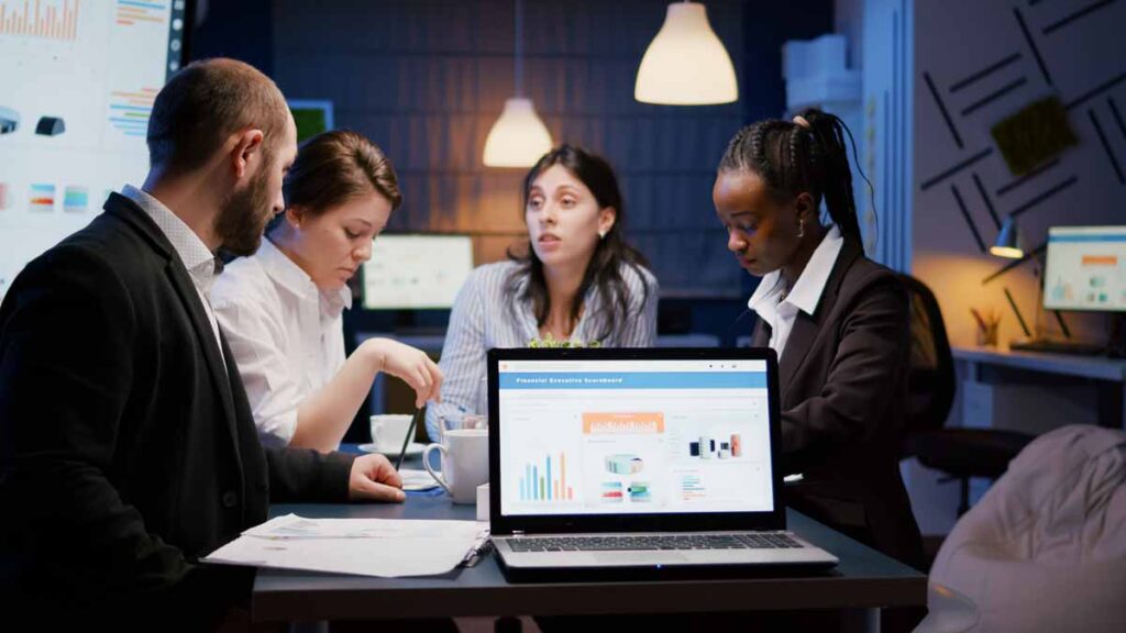 laptop computer with financial graphs presentation monitor standing conference table meeting room late night